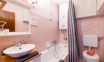 A bright bathroom with pink tiles and a bathtub. There is a washbasin and a shower with a curtain.