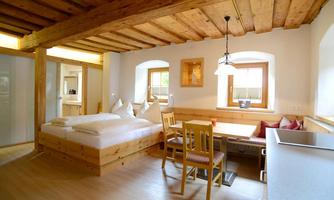 A cozy room with wooden ceilings, a double bed, and a small dining table. Large windows provide plenty of daylight and an inviting atmosphere.