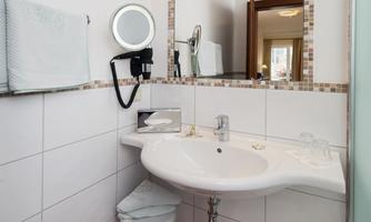 A modern bathroom with a sink, mirror, and towels. The walls are adorned with bright tiles and a decorative border.