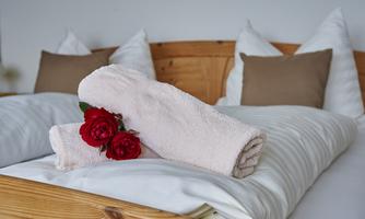 A cozy bed with bright pillows and a wooden frame. On the beds lie two towels and red roses.