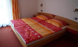 A cozy bedroom with a large double bed and colorful bedding. The room also has bright curtains that let in daylight.