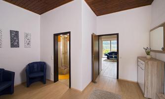 A bright entrance area with two comfortable blue chairs and modern decor. In the background, a room with access to the terrace can be seen.