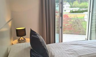 A cozy bedroom with two beds and modern pillows. Large windows provide a view of nature outside.