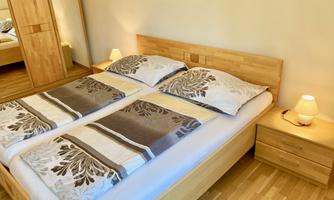 A bright bedroom with a double bed and wooden furniture. Next to the bed is a bedside table with a lamp.