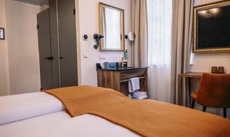 A modern bedroom with a large bed and an orange blanket. The room is bright and friendly, with a desk and a mirror.