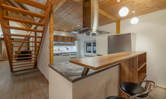 A modern kitchen with wooden cladding and an open bar. A staircase leads to the upper area of the room.