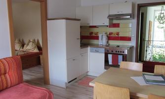 A modern kitchen with white furniture and colorful tiles. The room contains a dining table and a cozy seating area.