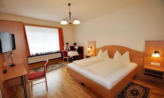 A cozy hotel room with a double bed, a desk, and a TV. There is a seating area with a table and two chairs.