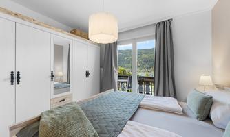 A bright bedroom with two beds and a modern furniture style. Large windows offer a view of the green landscape.