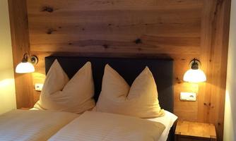 A cozy bedroom with a double bed and wooden paneling. Two nightstands with lights create a warm atmosphere.