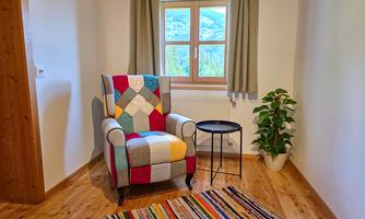 A cozy armchair with a colorful pattern is in a bright room. Next to the armchair is a small table and a green plant in a pot.