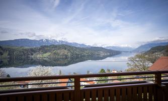 A picturesque landscape with a clear lake, surrounded by mountains and green shores. The sky is blue with some clouds.