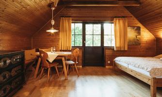 A cozy room with wooden paneling, a bed, and a dining area. Large windows let in plenty of light and provide a view outside.