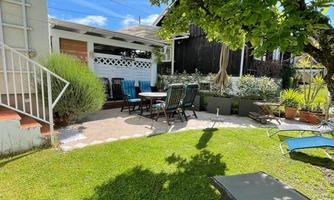 A cozy garden with a seating area, loungers, and a sunshade. The green spaces and the tree provide an inviting atmosphere.