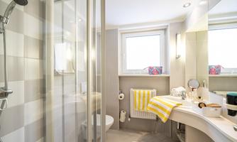 A modern bathroom with a shower and a large mirror. Bright colors and simple furnishings create an inviting atmosphere.