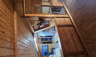 A cozy wooden house with an open living area. The walls and ceilings are made of wood, and there is a small kitchen and a dining area.