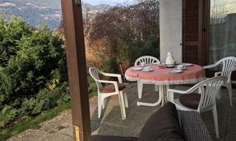 An inviting outdoor area with a table and chairs. In the background, green plants and a mountain landscape are visible.