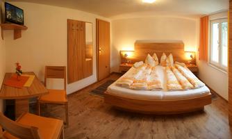 A cozy bedroom with a large bed and bright wood colors. There is a small table and chairs as well as a window with daylight.