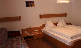 A cozy hotel room with a double bed and a couch. There is a lamp and some wooden furniture.