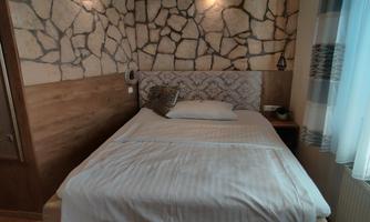 A cozy bedroom with a large bed and stone wall. There is plenty of daylight through the window.