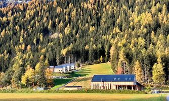A picturesque landscape with colorful autumn trees and two modern houses. The mountains in the background enhance the natural beauty of the surroundings.