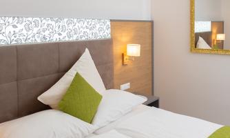 A modern bedroom with a comfortable double bed and a decorative headboard. The walls are painted in neutral colors, complemented by warm lighting and an elegant mirror.