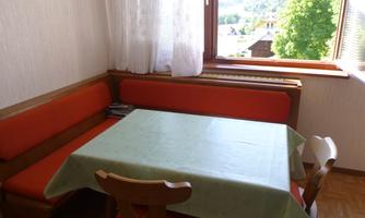 A cozy dining area with a green tablecloth and an L-shaped bench. A green landscape is visible through the window.
