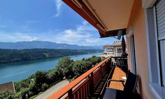 A beautiful view from a balcony of a clear river and green hills. The sun is shining in the blue sky.