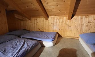 A simple room with wooden paneling and several beds. The mattresses have blue covers and the floor is uneven.