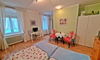 A cozy room with two beds and bright walls. There is a table with chairs and a desk in the corner.