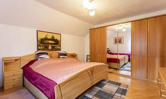 A cozy bedroom with a large bed and a wooden wardrobe. The walls are light, and a nice picture adorns the wall.