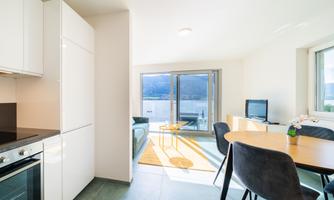 A modern apartment with a bright kitchen and a dining area. Large windows offer a view of the landscape and plenty of daylight.