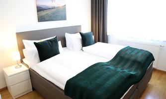A cozy bedroom with a double bed and modern bedding. The room has a large windowsill with plenty of daylight and a pretty landscape picture on the wall.