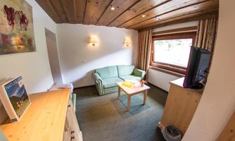 A cozy living space with a green sofa and a wooden table. On the wall, there are windows and a wooden ceiling that create an inviting atmosphere.