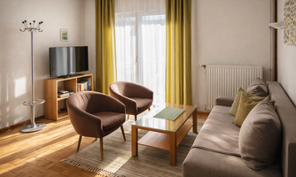 A modern living room with a bright color scheme. There is a sofa, two armchairs, and a television on a wooden shelf.