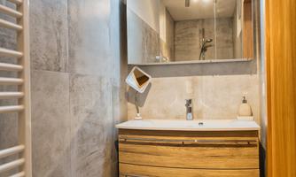 A modern bathroom with a wooden washstand and a large mirror. Towels are neatly stacked and a heater is installed on the wall.