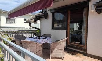 A beautiful balcony with a round table and wicker chairs. The awning is extended and there is a pleasant view of the surroundings.