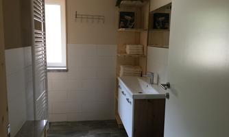 A bright bathroom with a modern vanity and shelves. There are towels and a large mirror.