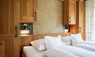 A cozy bedroom with a double bed and wooden furniture. The walls are warmly designed, and there are natural light sources.