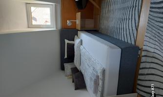 A cozy bedroom with a bed, a small table, and a desk. The room has a bright window front and a modern rug.