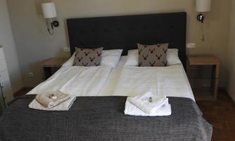 A cozy bedroom with a double bed and decorative pillows. On the nightstands are lamps and fresh towels.