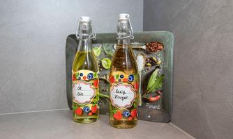 Two bottles with colorful labels are standing on a gray table. In the background, there is a tray with various foods.
