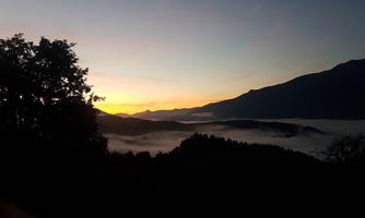 A beautiful sunrise over the mountains with gentle wisps of fog in the valley. The silhouettes of the trees add depth and tranquility to the scene.