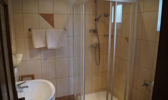 A modern bathroom with a shower and a sink. The walls are tiled and there are two towels hanging.