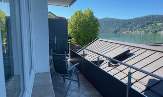 A balcony with a view of a lake and surrounding hills. The atmosphere is relaxing and calm.