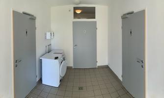 A hallway with several doors and a washing machine. Signs for private bathrooms hang on the walls.