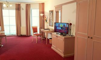 A bright room with a television, a table, and chairs. The walls are painted in soft colors, and the red carpet complements the cozy atmosphere.