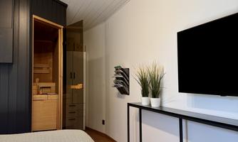 A modern bedroom with a large bed and a television on the wall. In the corner, there is access to a small bathroom or a sauna.