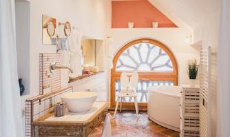 A modern bathroom with a round window front. It features an elegant bathtub, a sink, and a wooden shelf.
