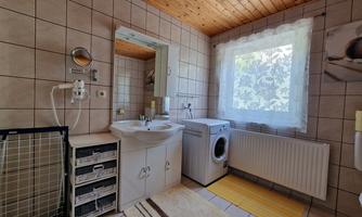 A modern bathroom with a large window and a washing machine. There are bright tiles and a wooden ceiling that give the room a cozy atmosphere.